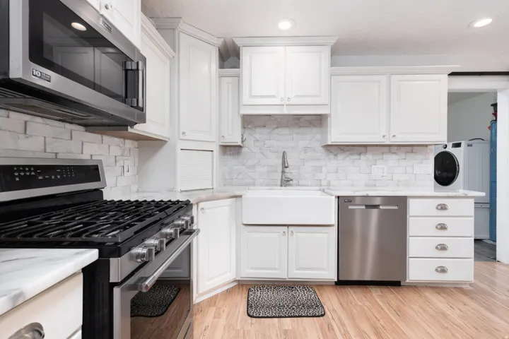 Kitchen with stainless steel appliances, white cabinetry, light stone countertops, light wood finished floors, and washer / clothes dryer