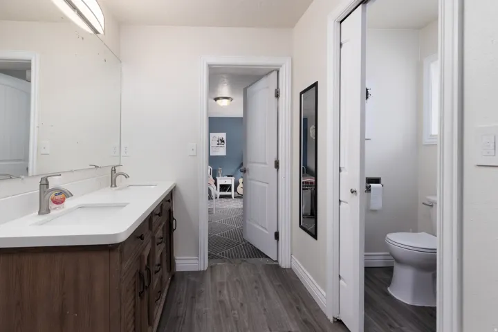 Full bathroom featuring double vanity and dark wood-type flooring