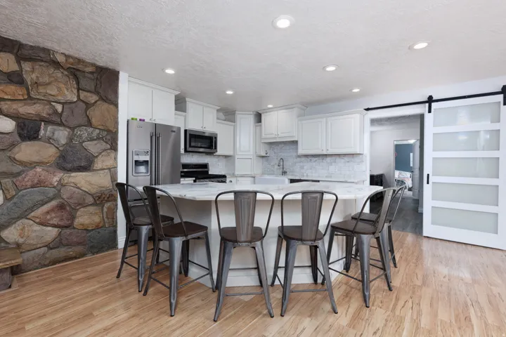 Kitchen featuring a barn door, white cabinets, light stone countertops, light wood-style floors, and decorative backsplash