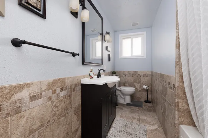 Full bathroom featuring tile walls, a wainscoted wall, and vanity