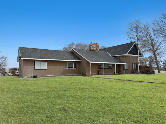 View of front of home with a shingled roof, a front lawn, stucco siding, a chimney, and covered porch