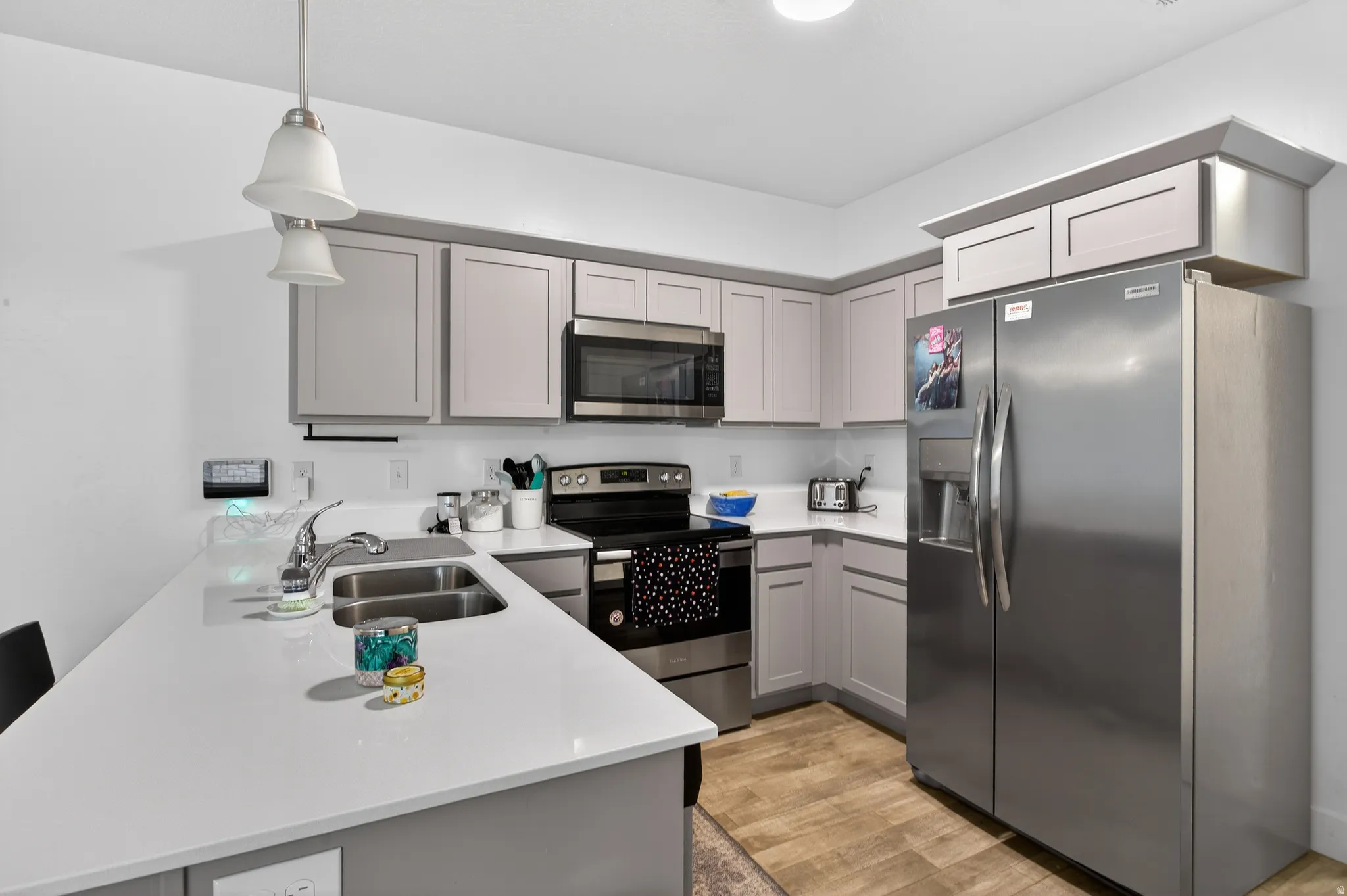 Kitchen with stainless steel appliances, gray cabinetry, a peninsula, light wood-type flooring, and hanging light fixtures