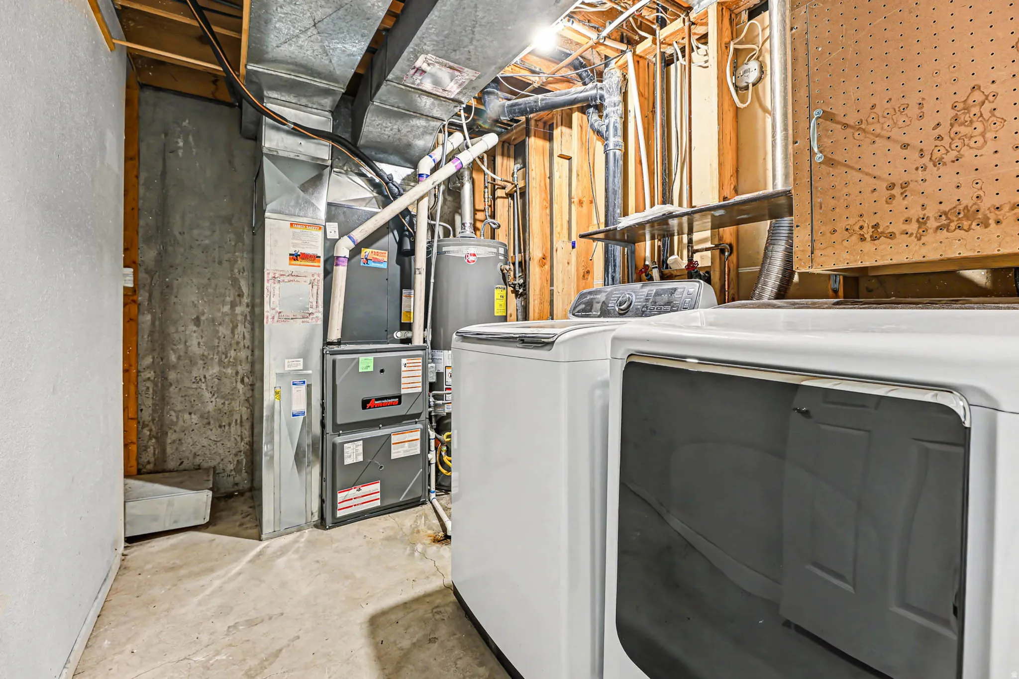 Laundry area with unfinished concrete floors, gas water heater, independent washer and dryer, and heating unit