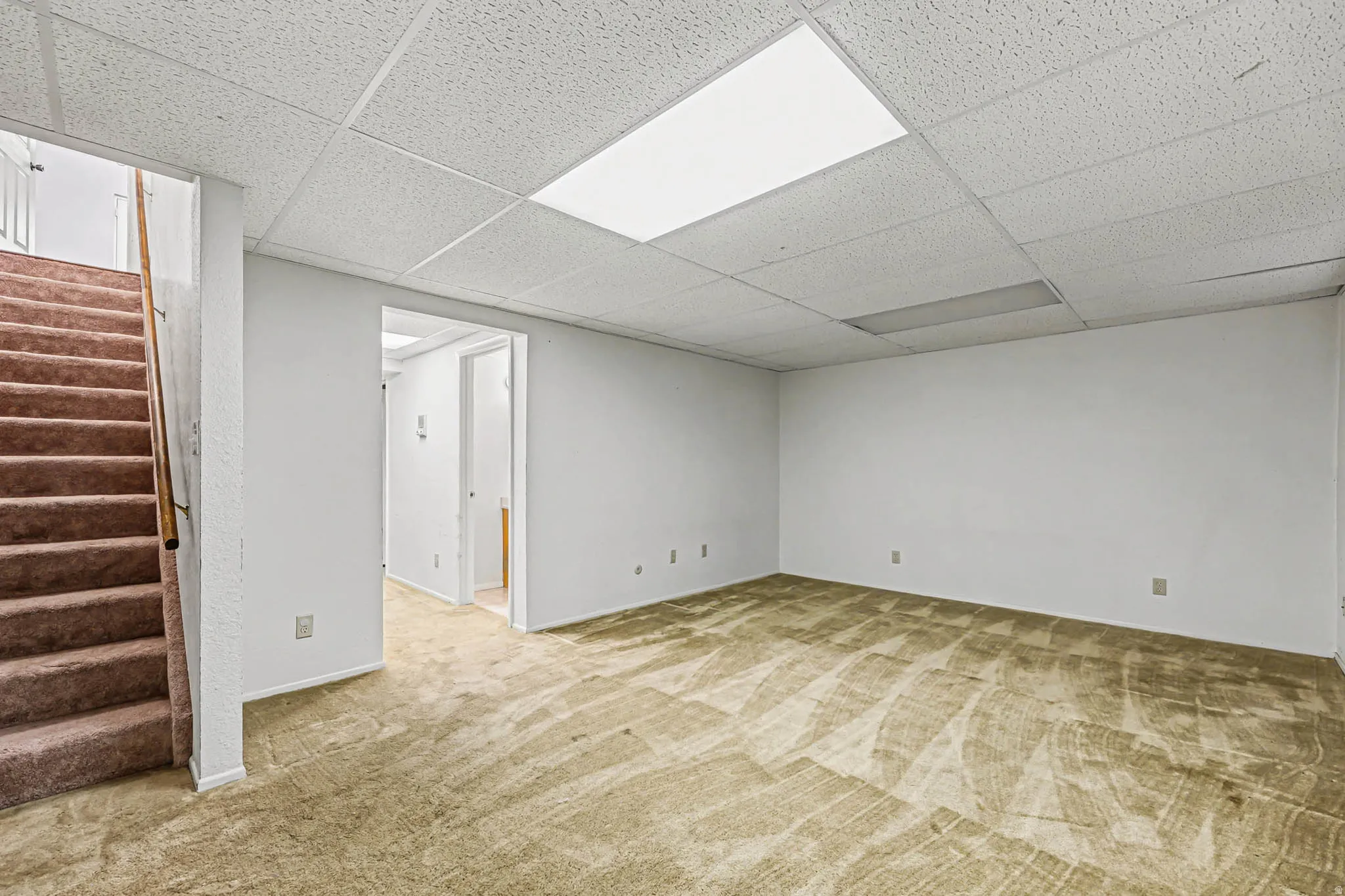Finished basement with light colored carpet and a drop ceiling