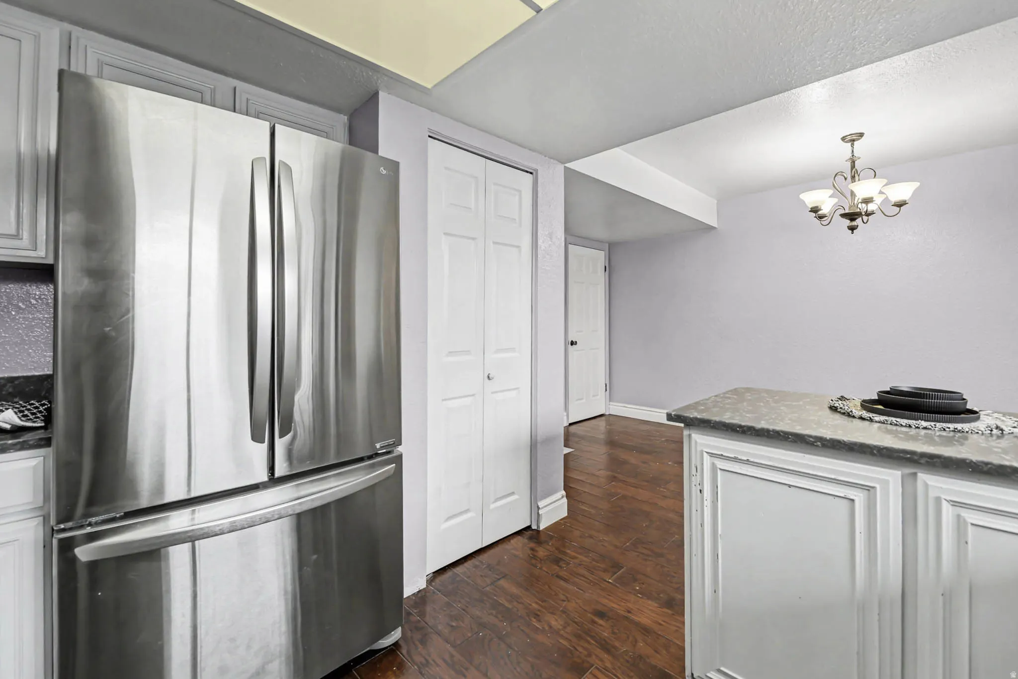 Kitchen featuring freestanding refrigerator, dark wood finished floors, suspended lighting, dark stone counters, and white cabinets