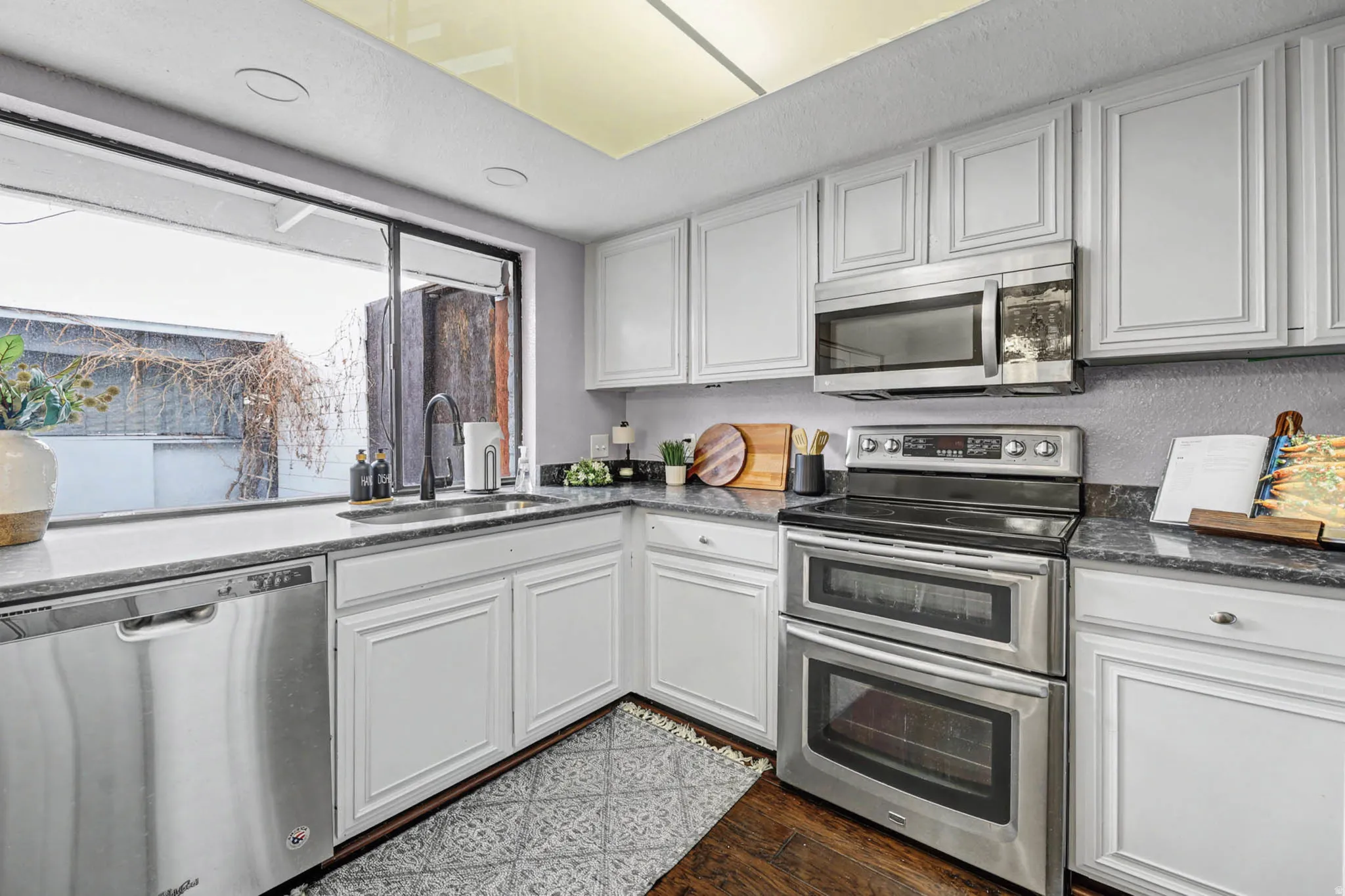 Kitchen with stainless steel appliances, dark stone counters, and white cabinetry