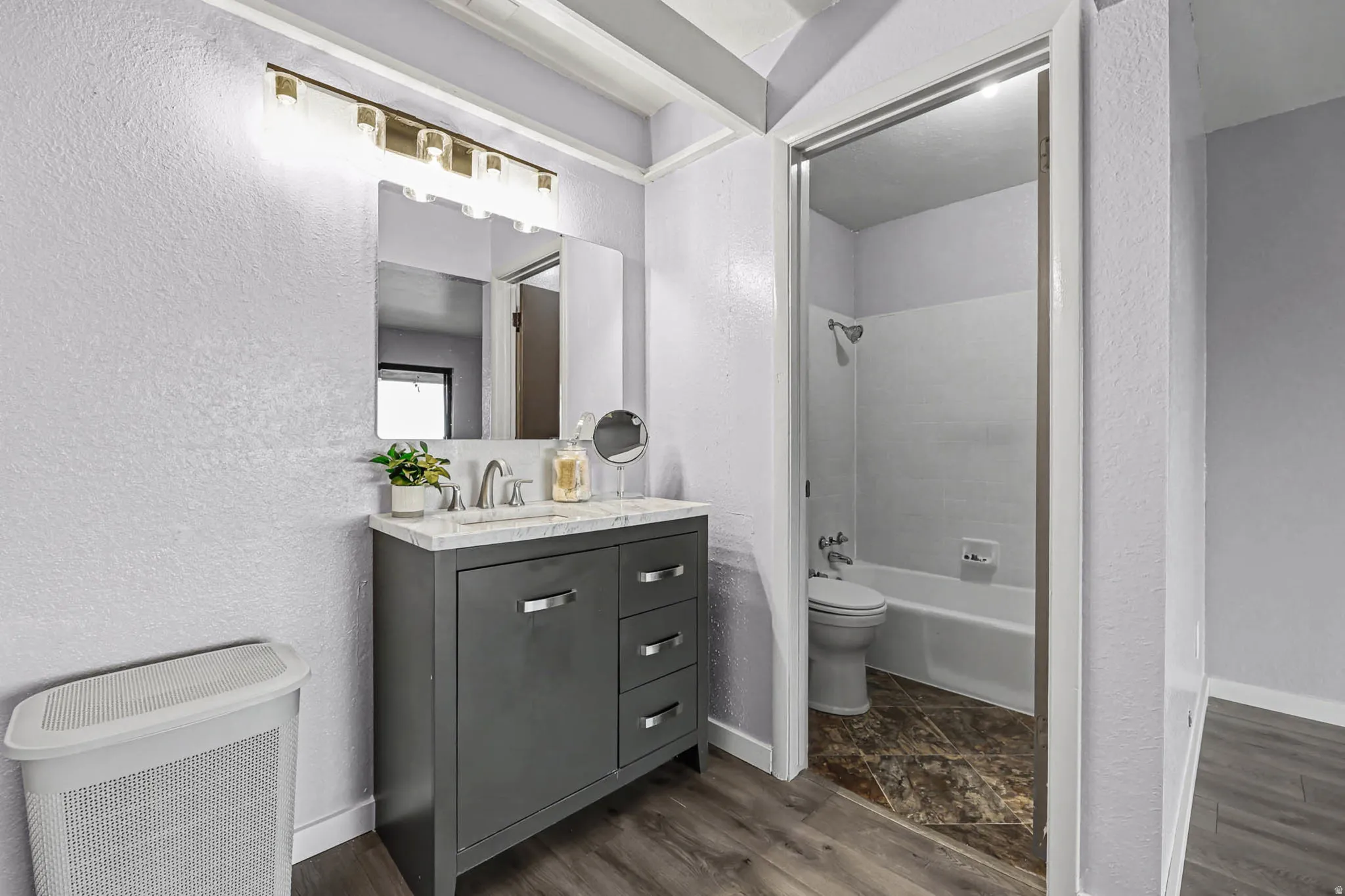 Full bath with a textured wall, bathtub / shower combination, dark wood-type flooring, and vanity