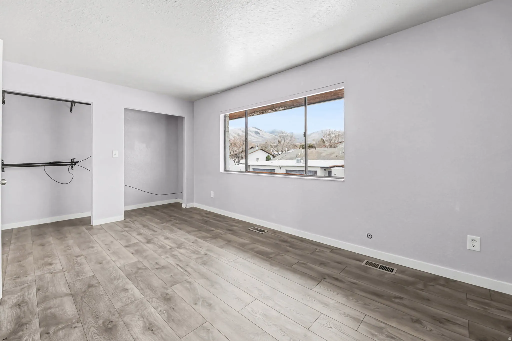Unfurnished bedroom with light wood finished floors, a textured ceiling, and two closets