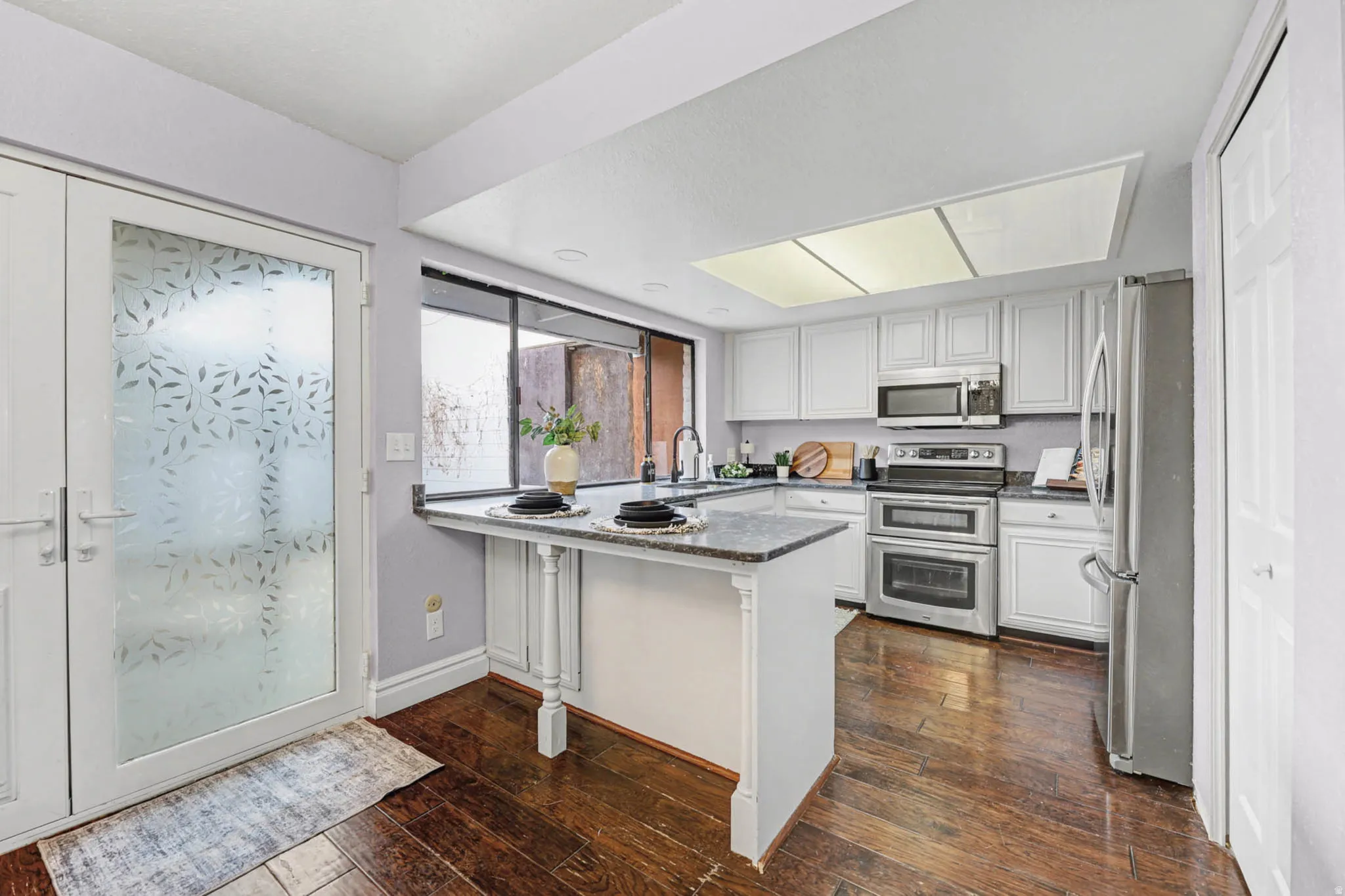 Kitchen with stainless steel appliances, dark wood finished floors, a peninsula, white cabinets, and dark stone countertops