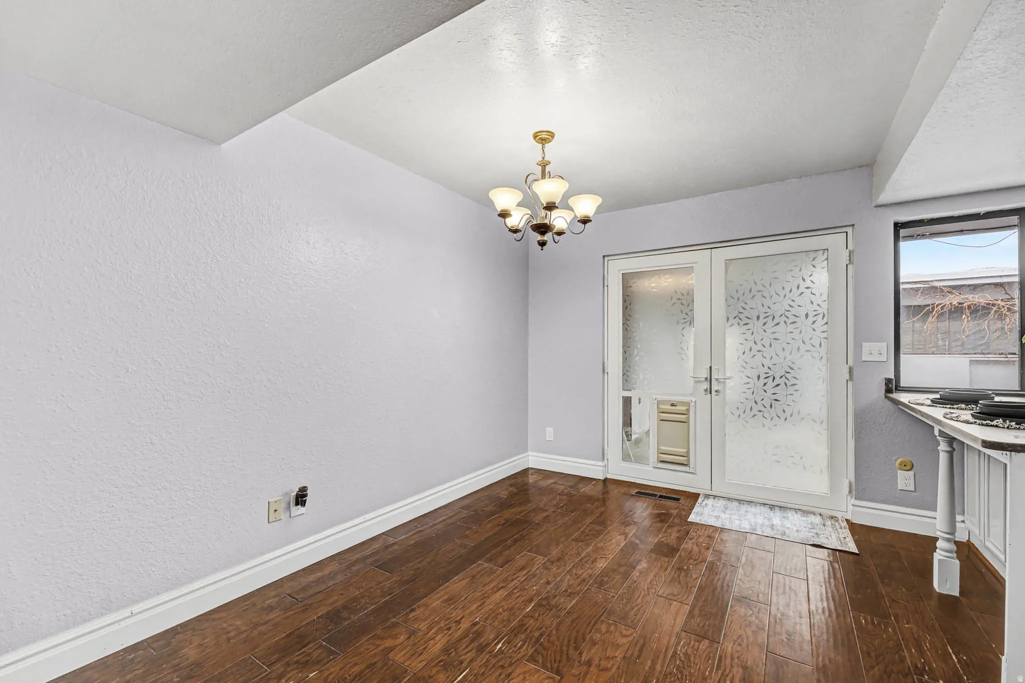 Unfurnished dining area featuring a textured wall, suspended lighting, dark wood-style floors, french doors, and a textured ceiling