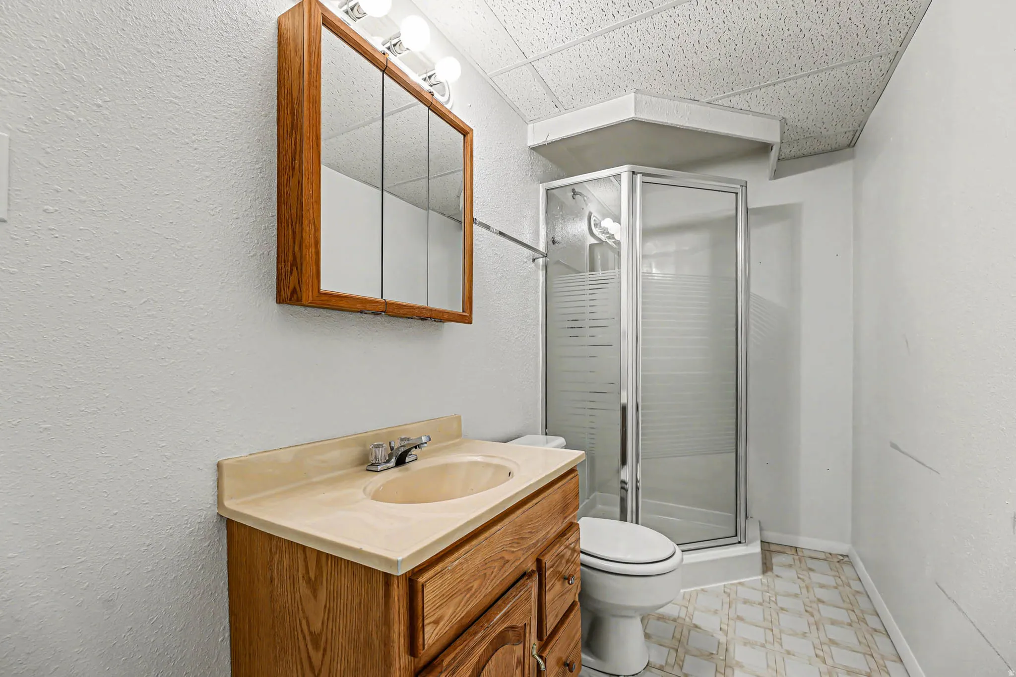 Bathroom featuring a shower stall, light flooring, a paneled ceiling, vanity, and a textured wall
