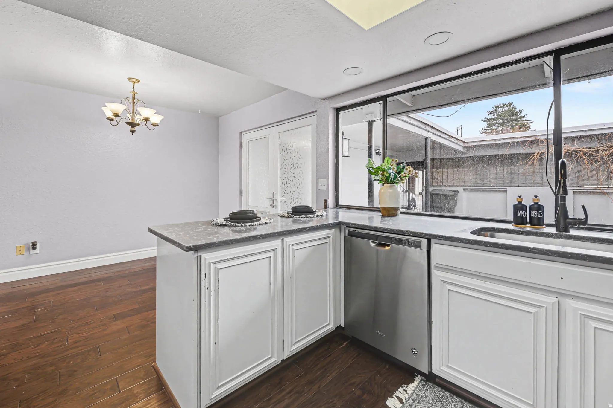 Kitchen with a peninsula, white cabinets, dishwasher, dark wood finished floors, and dark stone countertops