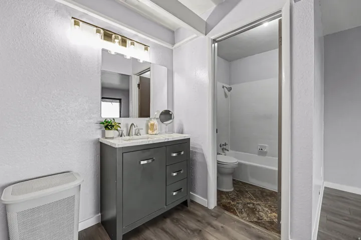 Full bath with a textured wall, bathtub / shower combination, dark wood-type flooring, and vanity