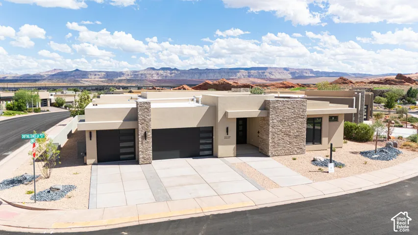 Modern architecture featuring a stucco exterior, stone accent columns, flat roofline, and integrated garage doors