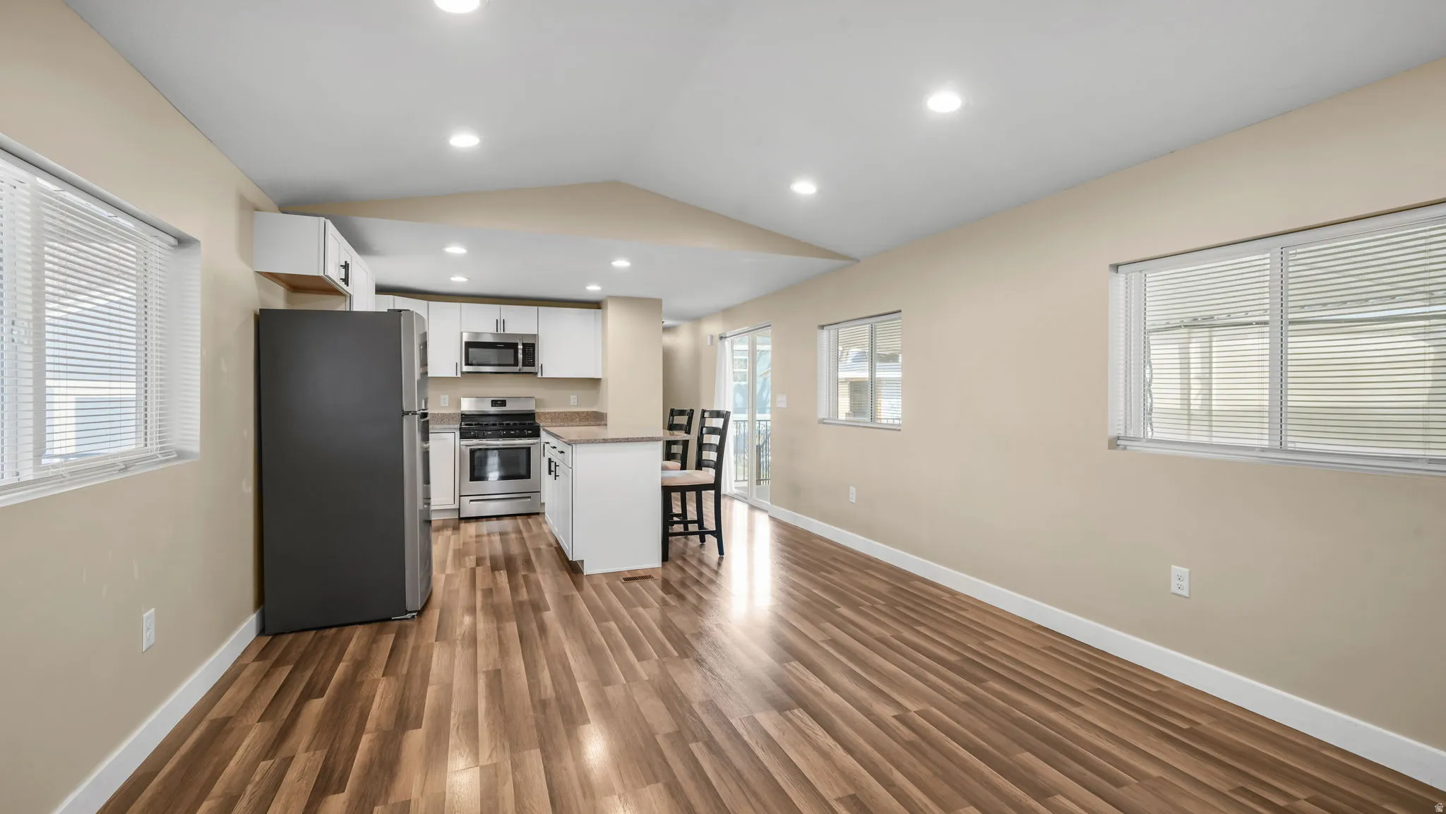 Kitchen with stainless steel appliances, white cabinets, a kitchen bar, lofted ceiling, and dark wood finished floors