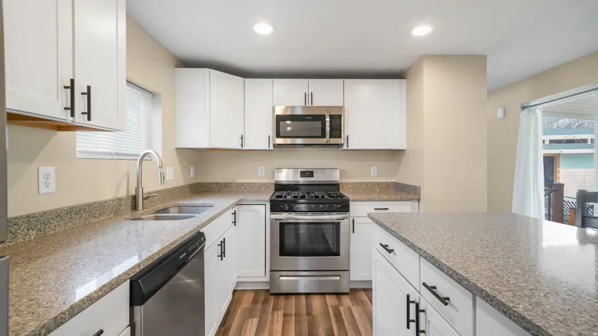 Kitchen with stainless steel appliances, white cabinetry, light stone countertops, and recessed lighting
