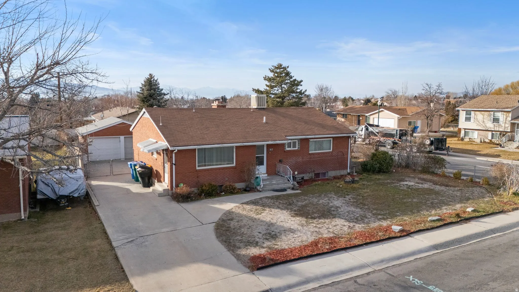 View of front facade with a chimney, brick siding, an outdoor structure, concrete driveway, and a residential view