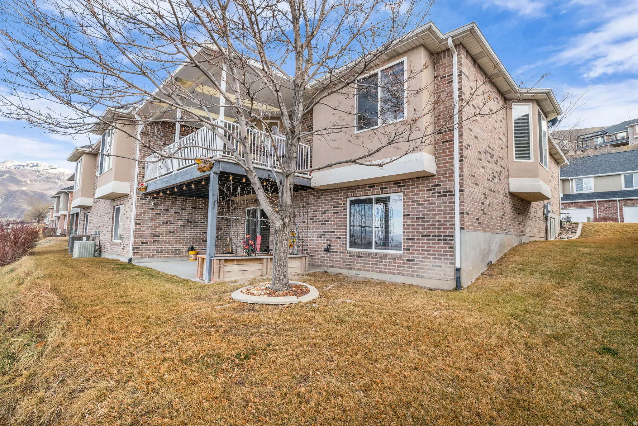 Back of house with a lawn, a patio, brick siding, and a deck with mountain view