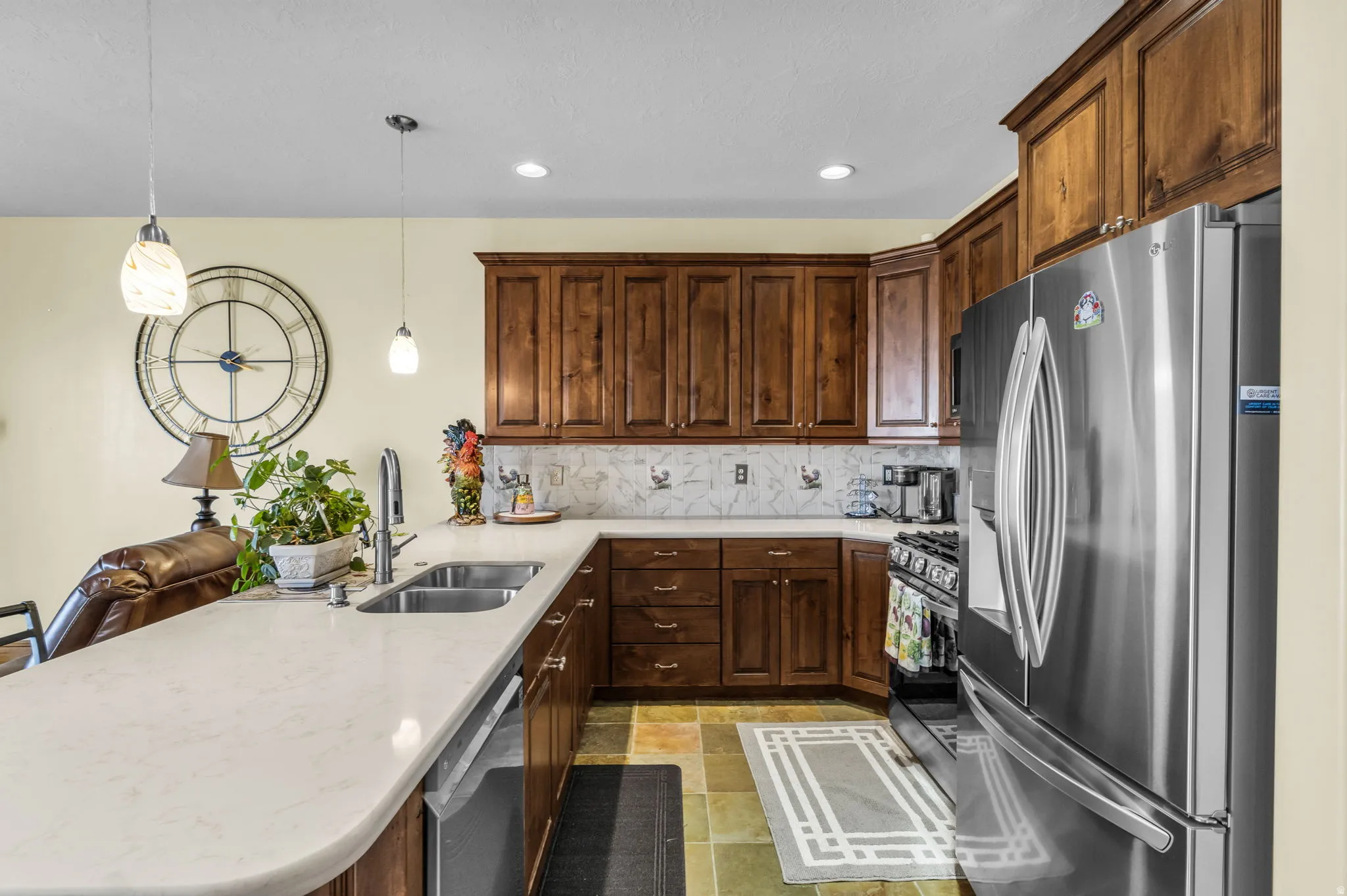 Kitchen featuring stainless steel appliances, a peninsula, pendant lighting, light stone finish flooring, and light stone counters