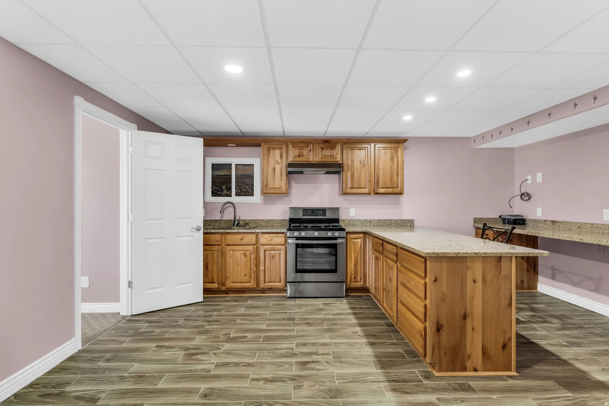 Kitchen featuring a peninsula, stainless steel range with gas stovetop, wood tiled floors, wood finish cabinetry, and light stone counters