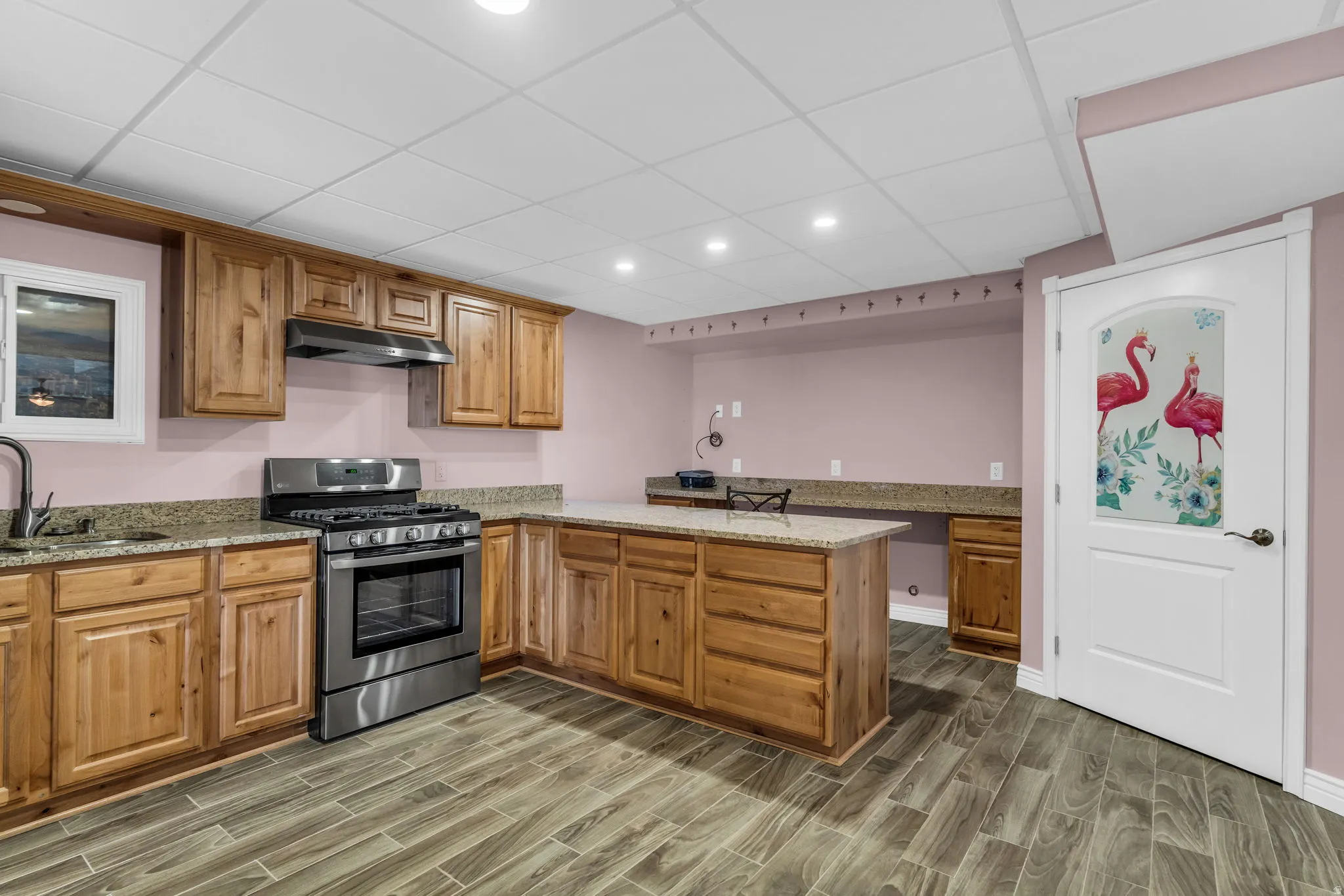 Kitchen with a peninsula, stainless steel range with gas stovetop, light stone counters, a paneled ceiling, and wood tiled floors