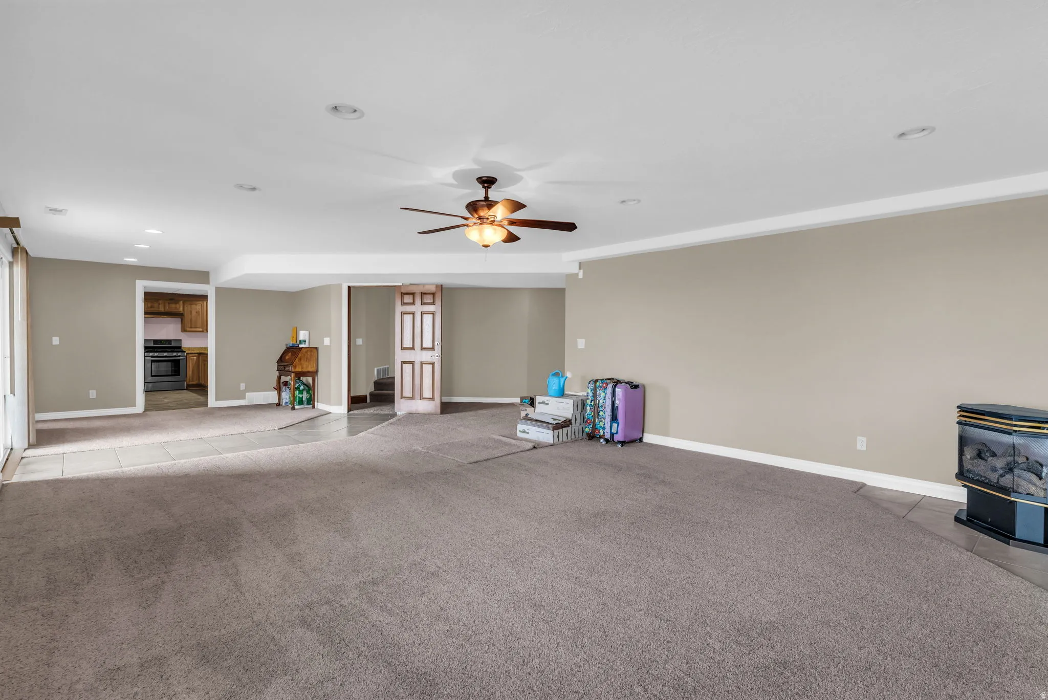 Unfurnished living room with ceiling fan, a wood stove, light carpet, and recessed lighting