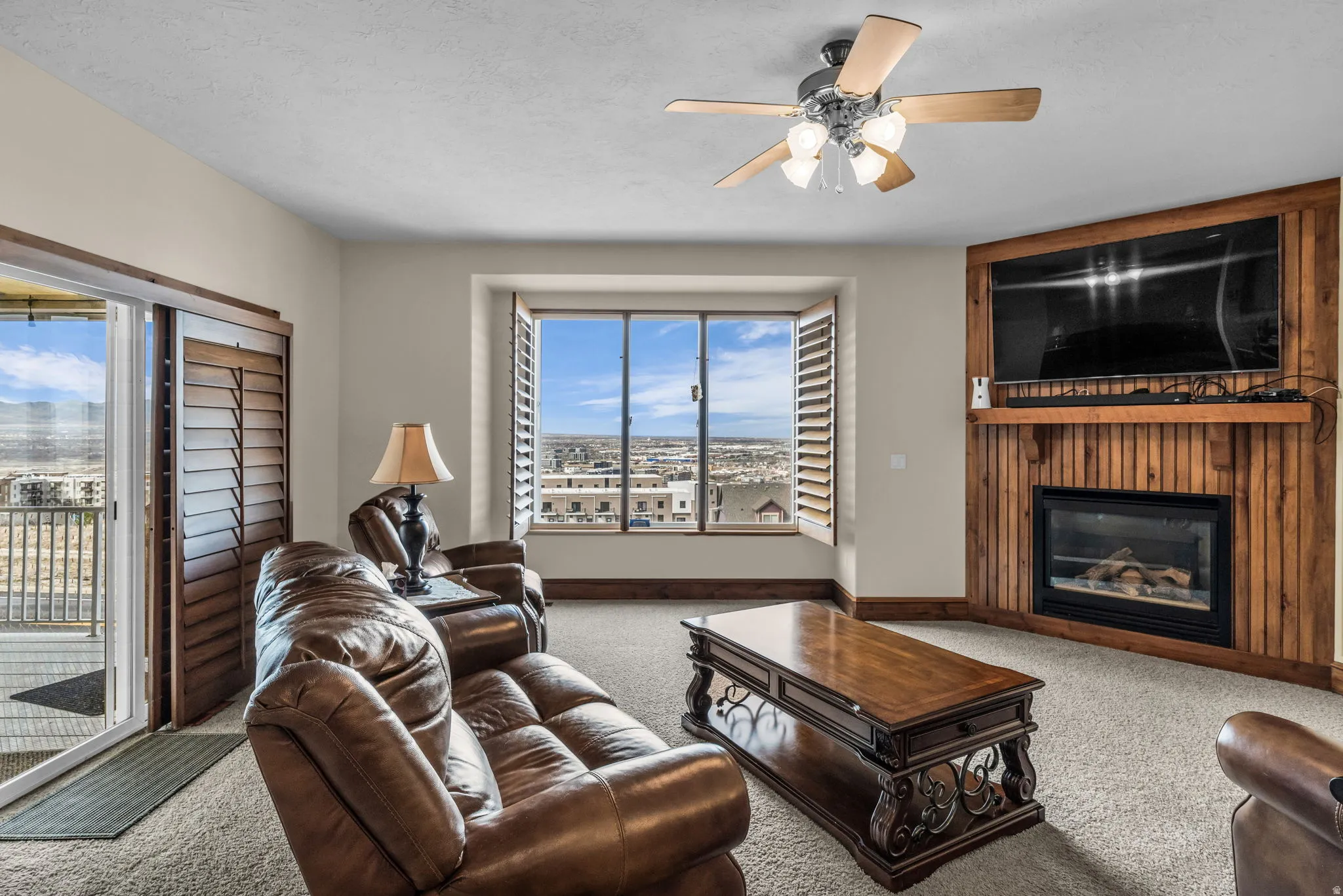 Living room featuring carpet flooring, a glass covered fireplace, ceiling fan, and a textured ceiling