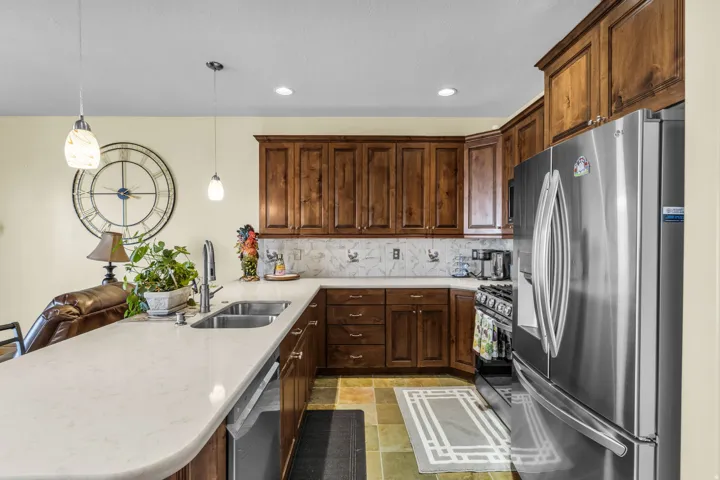 Kitchen featuring stainless steel appliances, a peninsula, pendant lighting, light stone finish flooring, and light stone counters