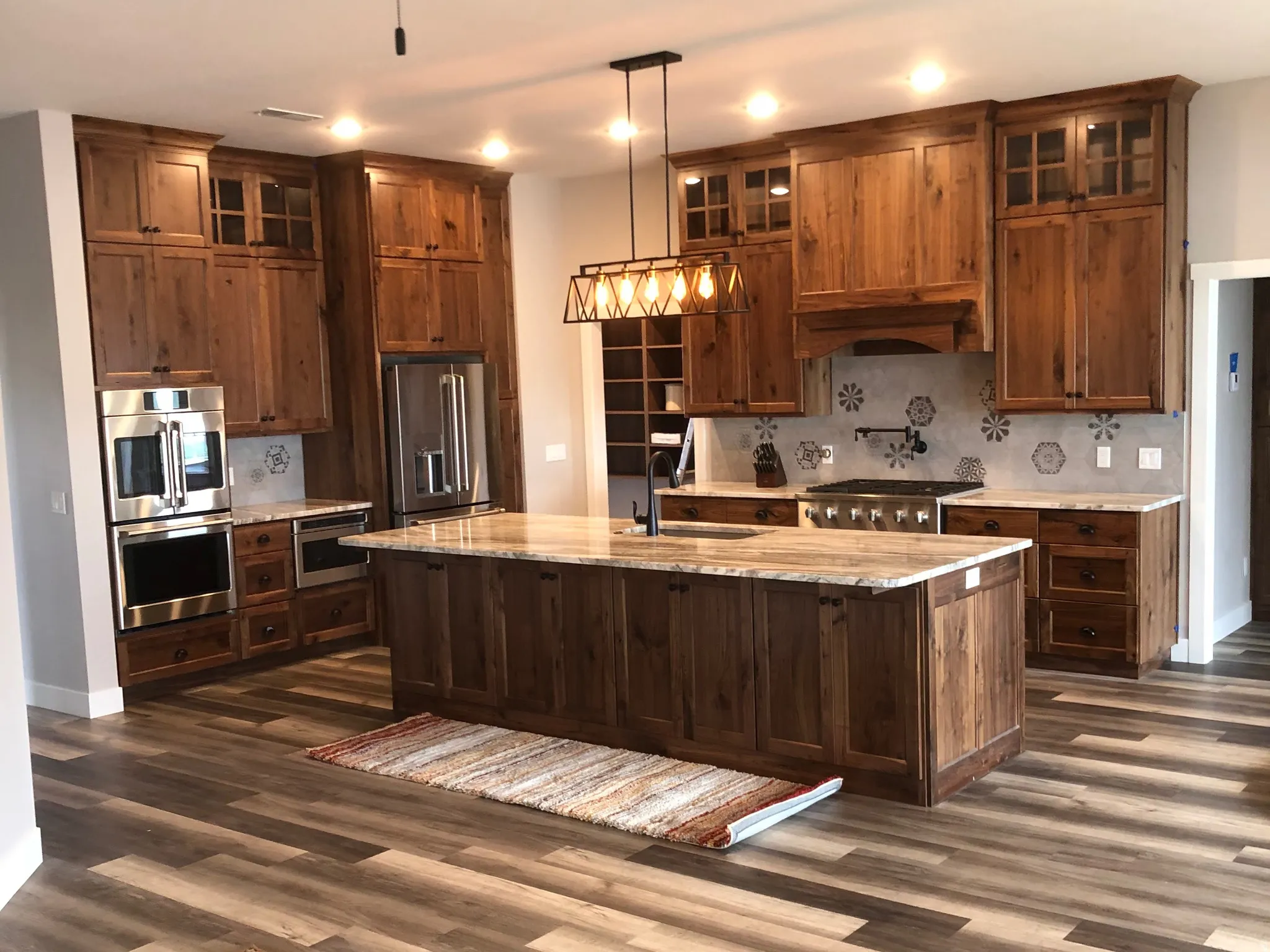 Kitchen with glass fronted cabinets, an island with sink, a ceiling fan, stainless steel appliances, and dark wood-style floors