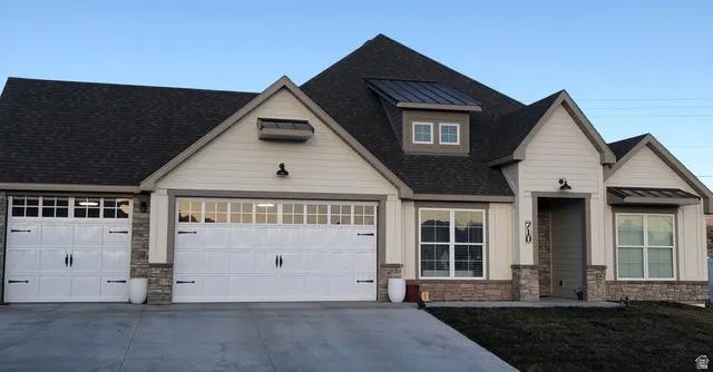 View of front of home featuring stone siding, driveway, an attached garage, and a standing seam roof