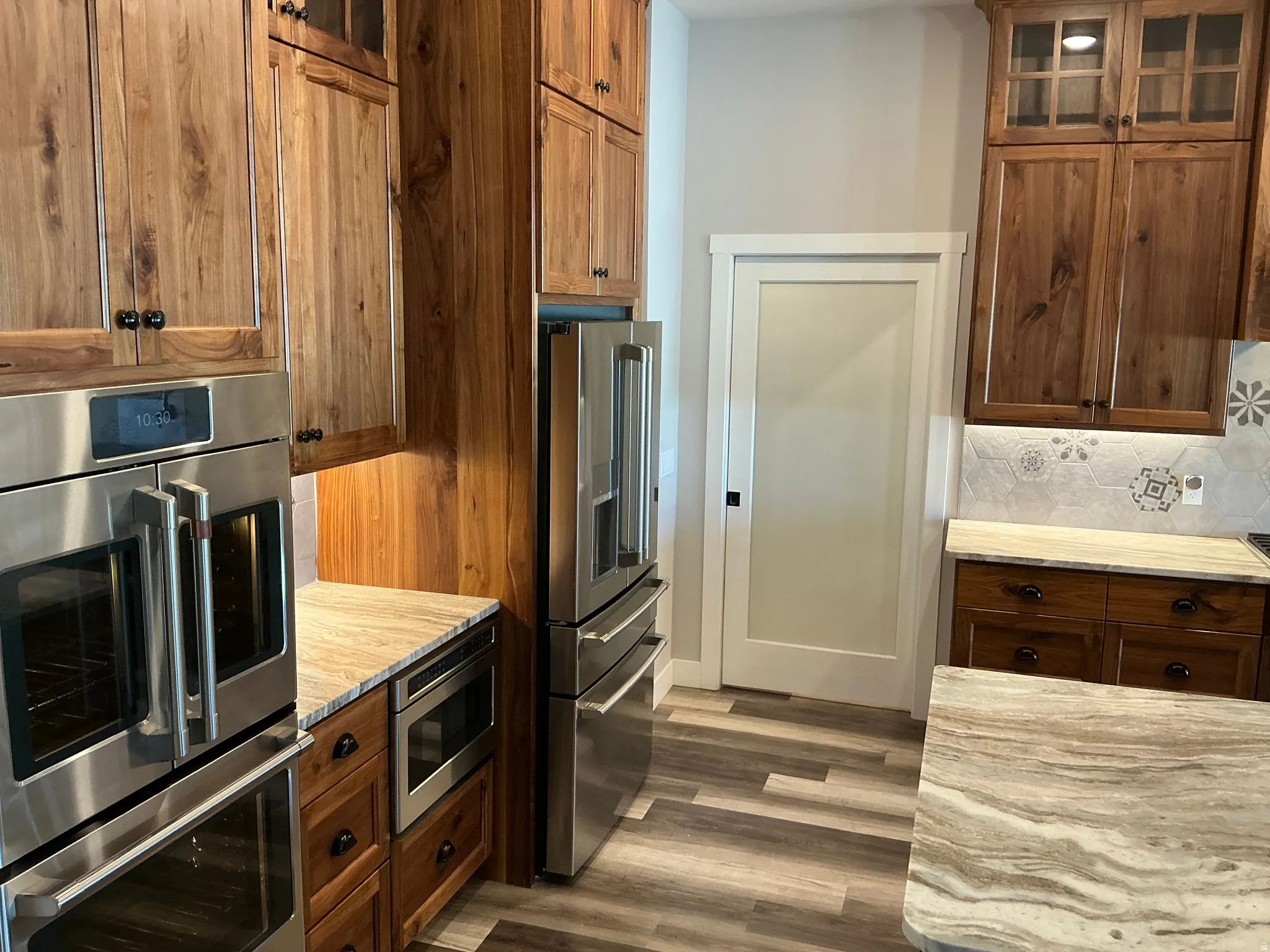 Kitchen featuring stainless steel appliances, glass fronted cabinets, light stone counters, and wood finish cabinetry