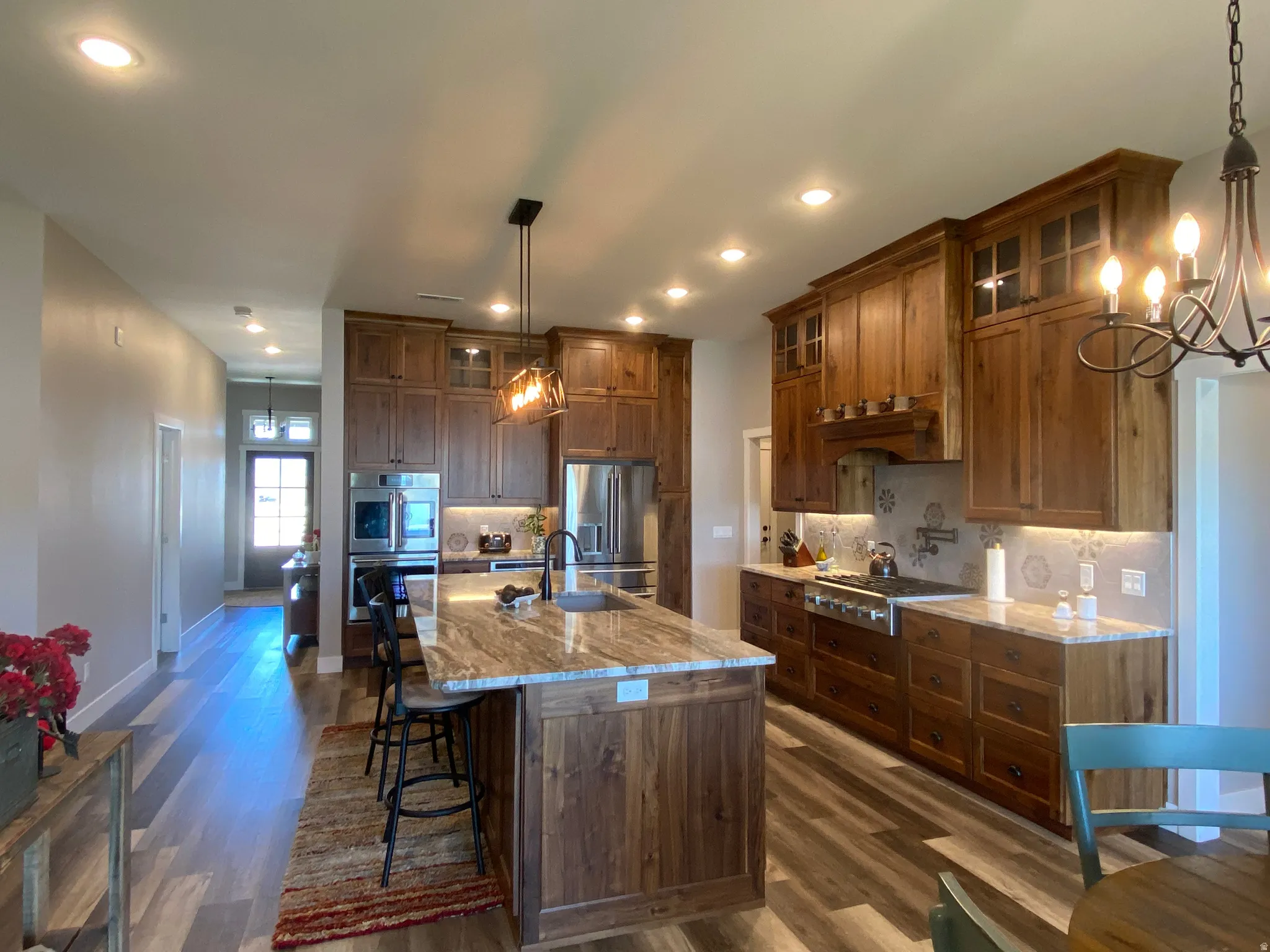 Kitchen with glass insert cabinets, light stone counters, suspended lighting, a breakfast bar area, and decorative backsplash