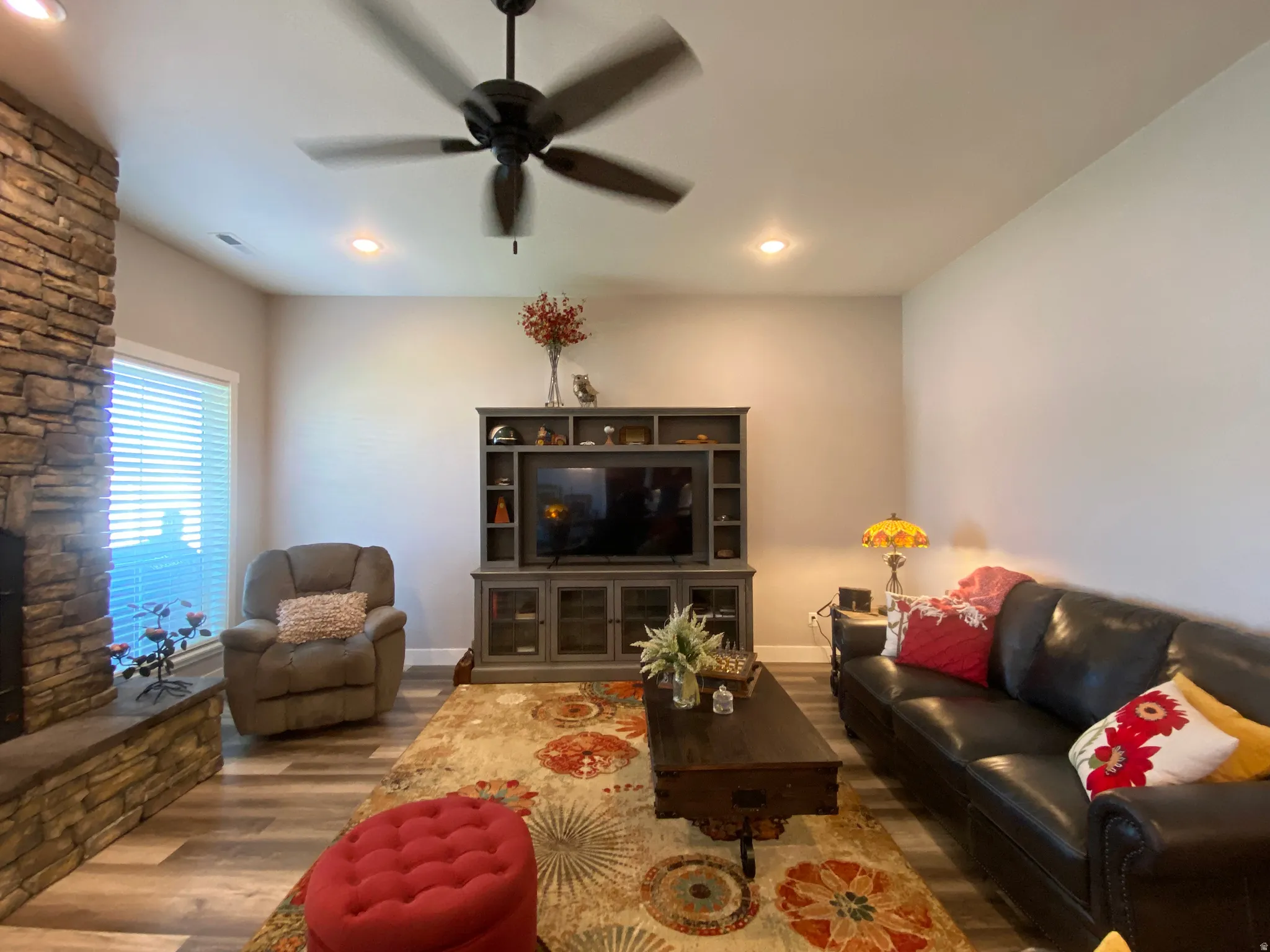 Living room featuring wood finished floors, a stone fireplace, ceiling fan, and recessed lighting