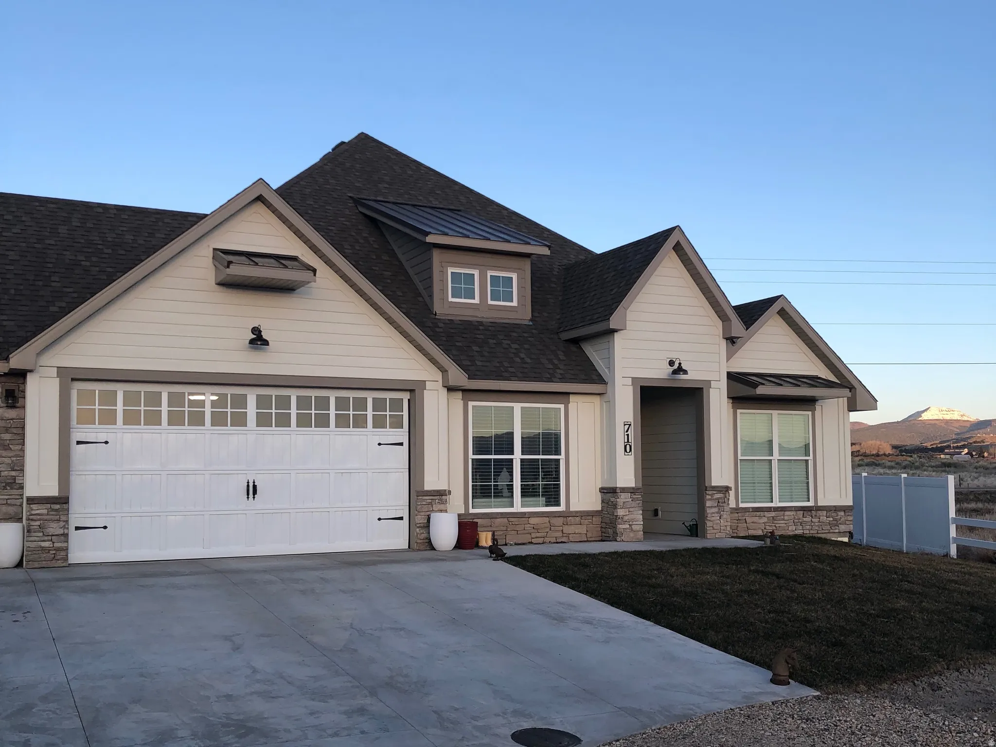 View of front of home featuring stone siding, driveway, a shingled roof, and an attached garage