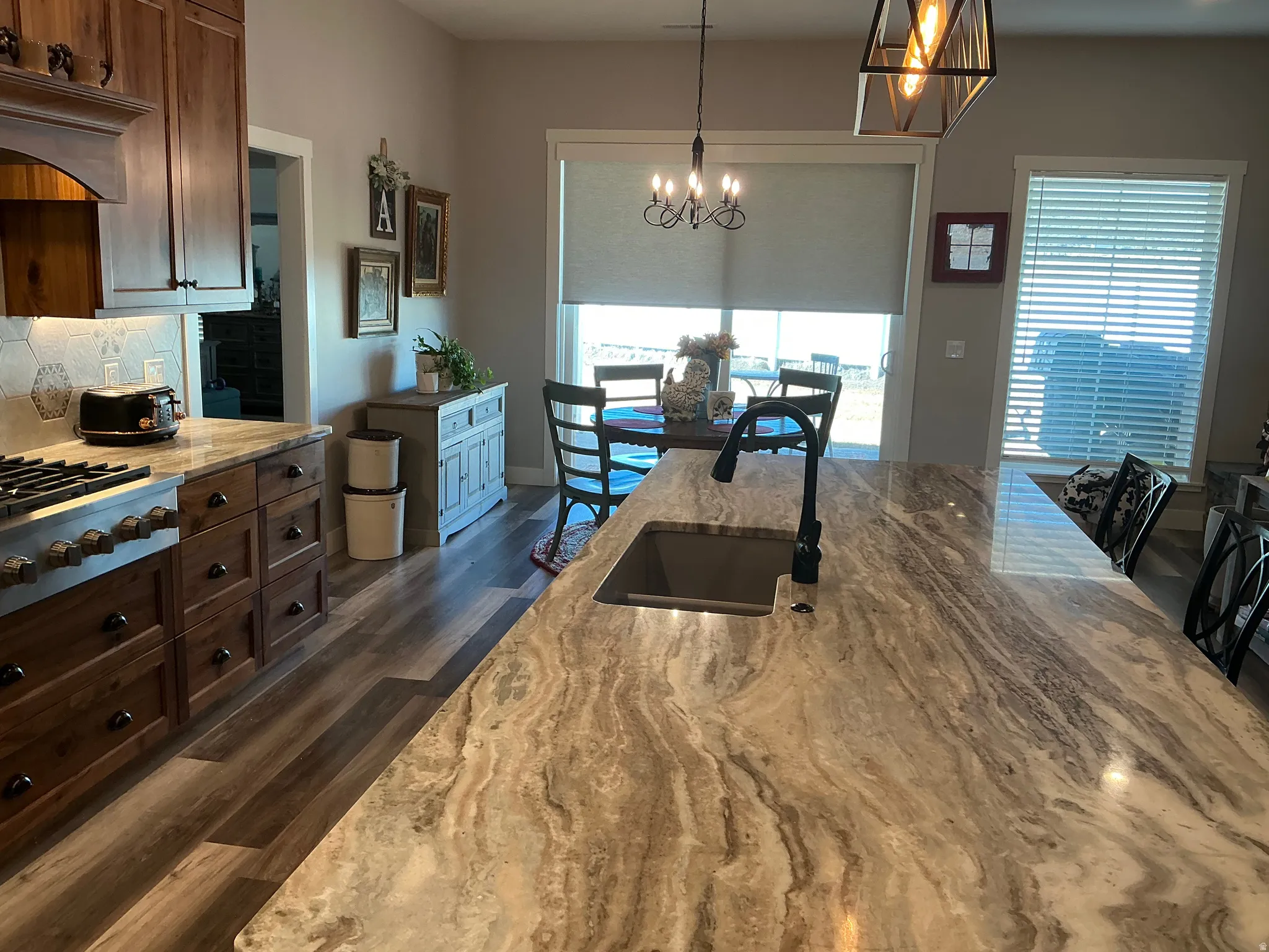 Two tone kitchen featuring light stone counters, dark wood finished floors, tasteful backsplash, stainless steel gas stovetop, and a chandelier