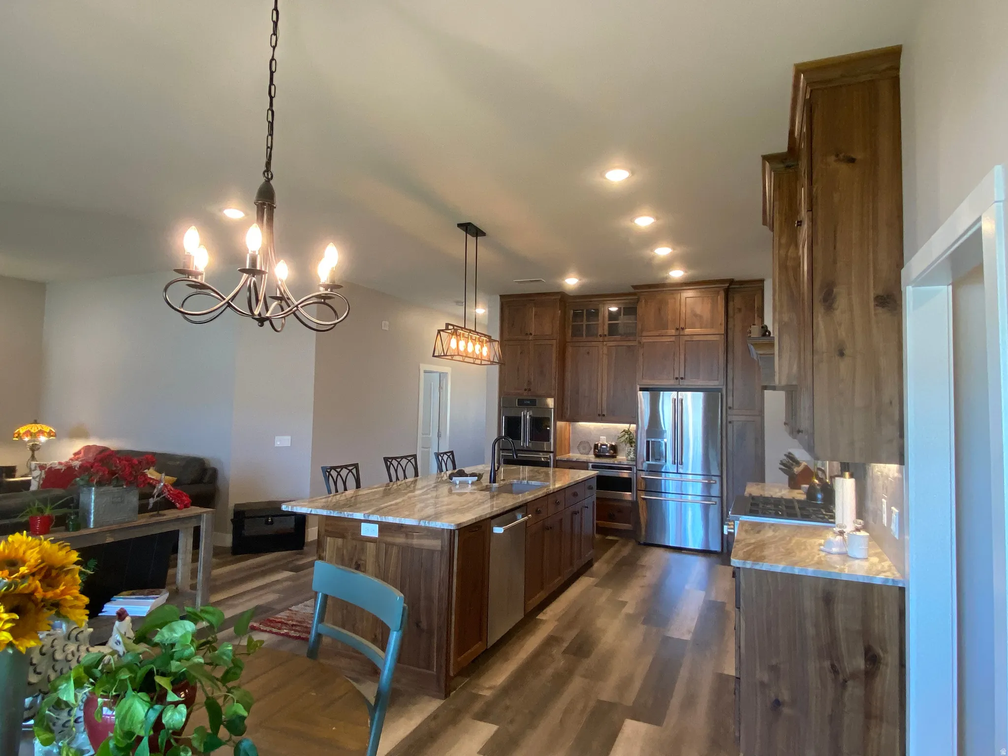 Kitchen featuring stainless steel appliances, glass insert cabinets, dark wood-style floors, hanging lights, and light stone counters