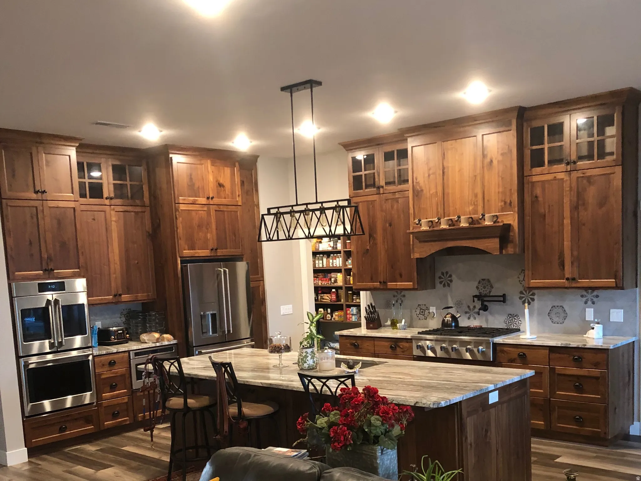 Kitchen featuring glass fronted cabinets, dark wood finished floors, a center island, hanging light fixtures, and light stone countertops