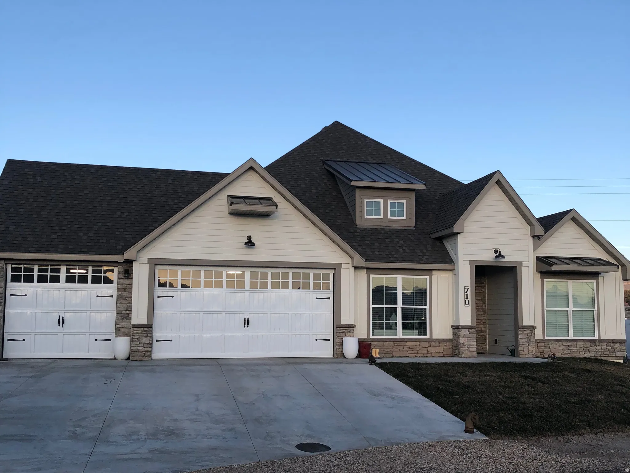 View of front facade featuring stone siding, driveway, a shingled roof, and an attached garage