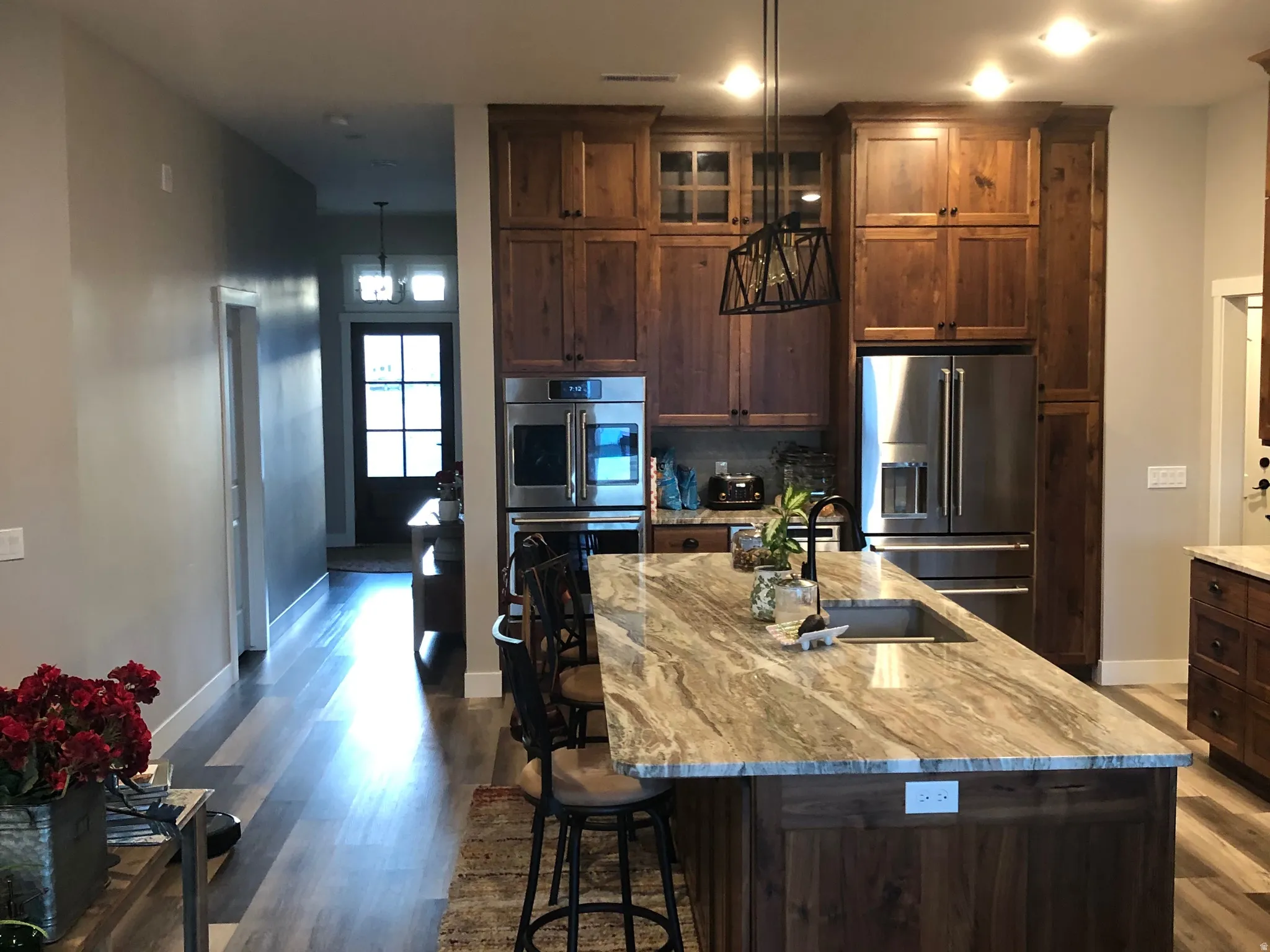 Kitchen with dark wood finish cabinets, an island with sink, light stone countertops, and stainless steel appliances
