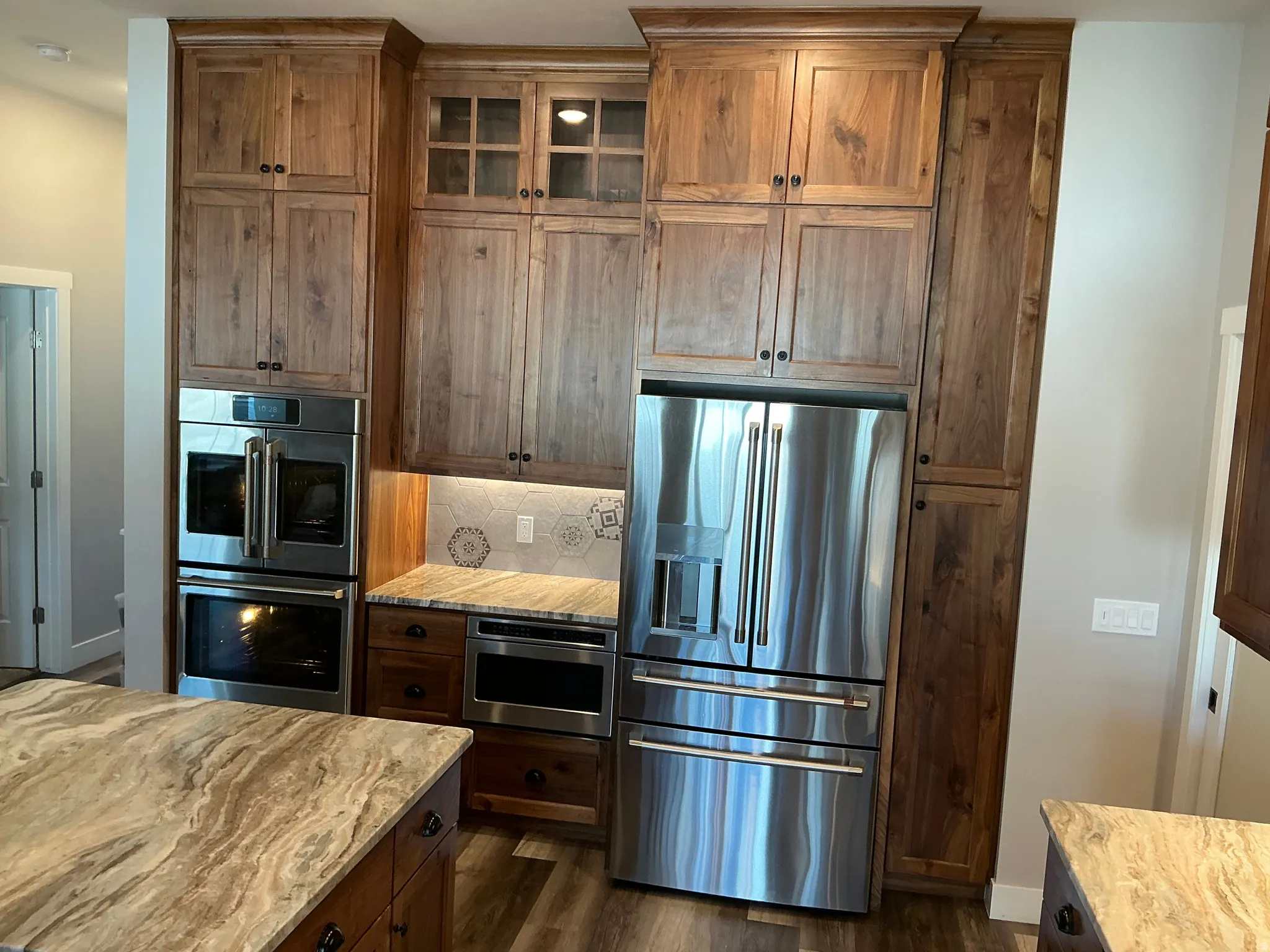 Kitchen with stainless steel appliances, glass insert cabinets, light stone counters, and dark wood finished floors