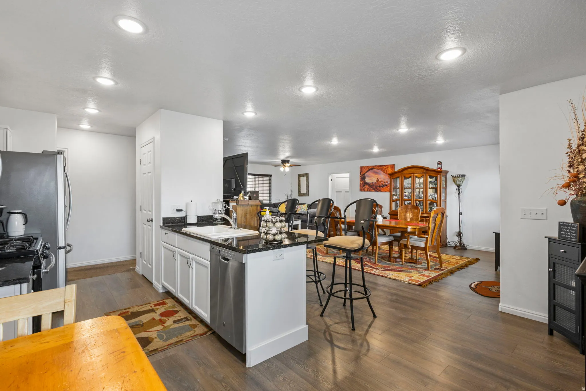 Kitchen with a peninsula, dark wood-style flooring, a kitchen bar, white cabinetry, and dark stone counters