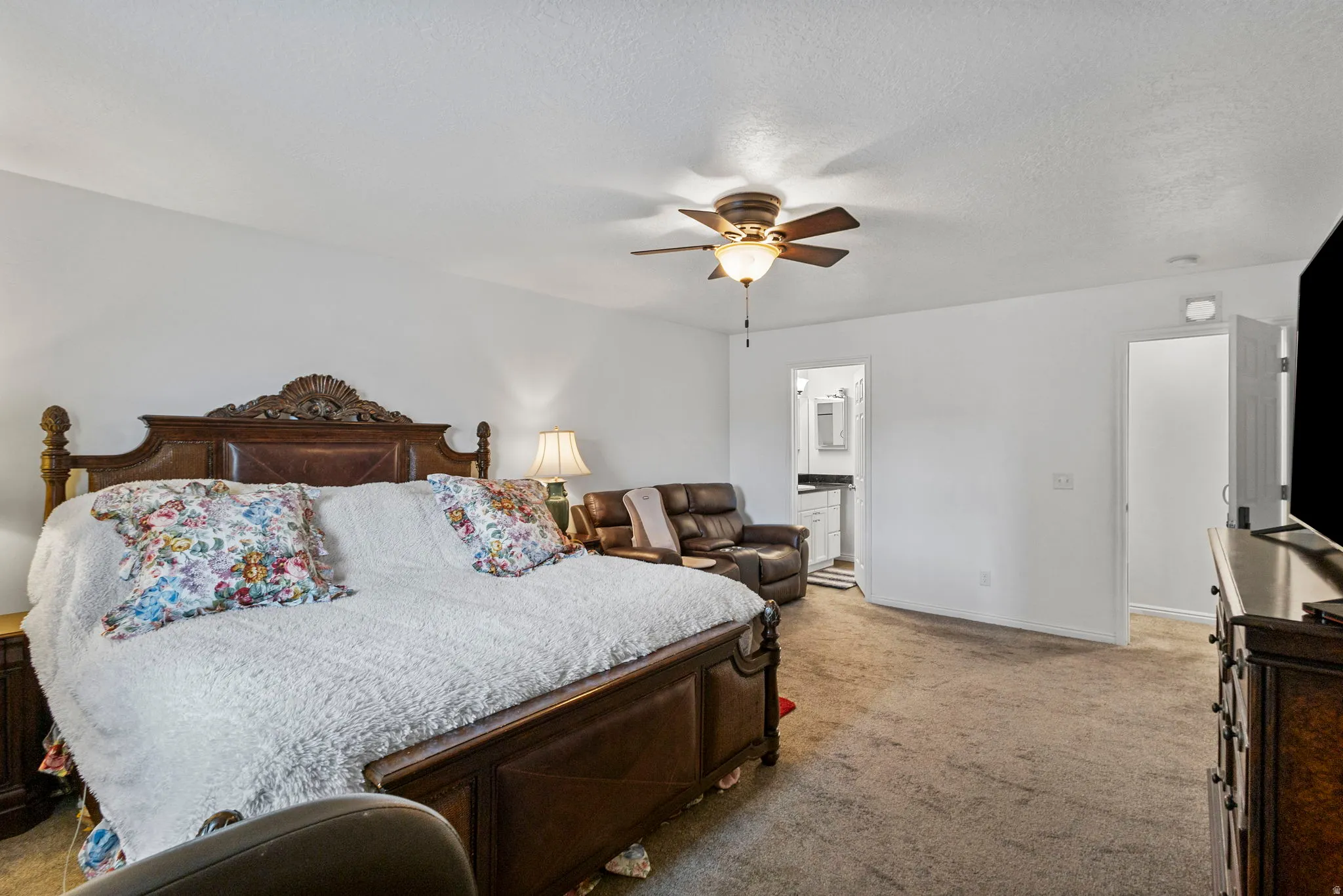Bedroom with light colored carpet, ceiling fan, a textured ceiling, and ensuite bathroom