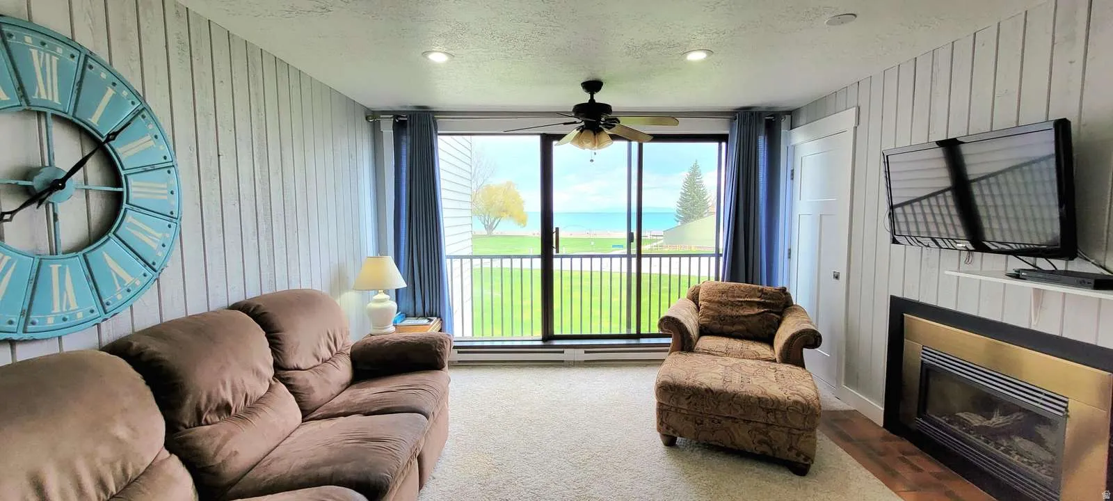 Living area with wooden walls, ceiling fan, a textured ceiling, carpet floors, and a glass covered fireplace