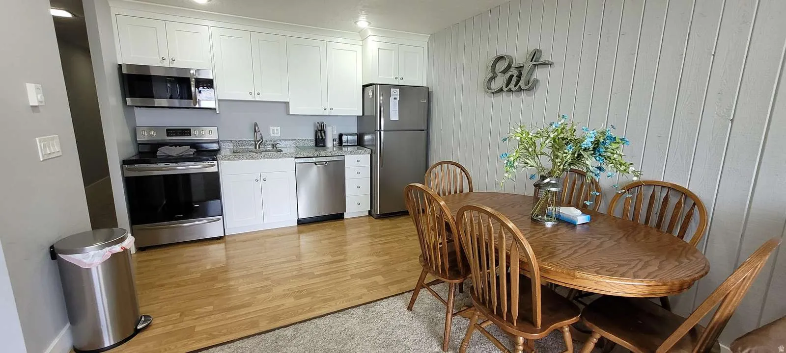 Kitchen with stainless steel appliances, white cabinets, wood walls, light wood-style flooring, and light stone counters