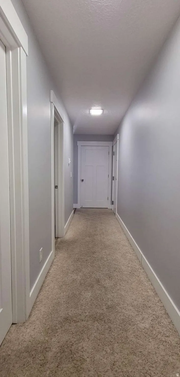 Corridor featuring light colored carpet and a textured ceiling