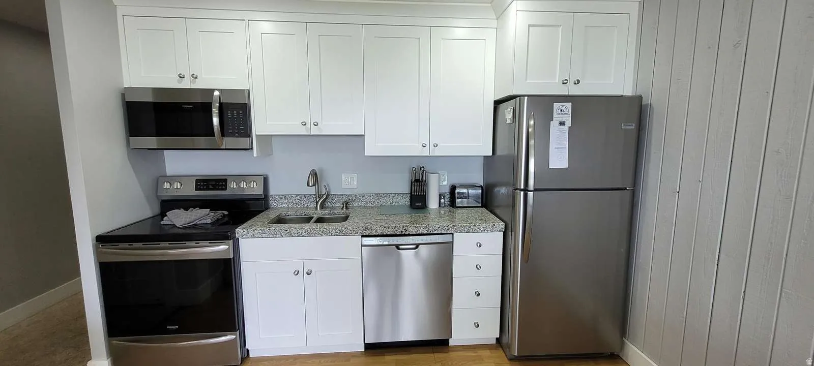 Kitchen featuring stainless steel appliances, white cabinetry, light stone countertops, and light wood finished floors