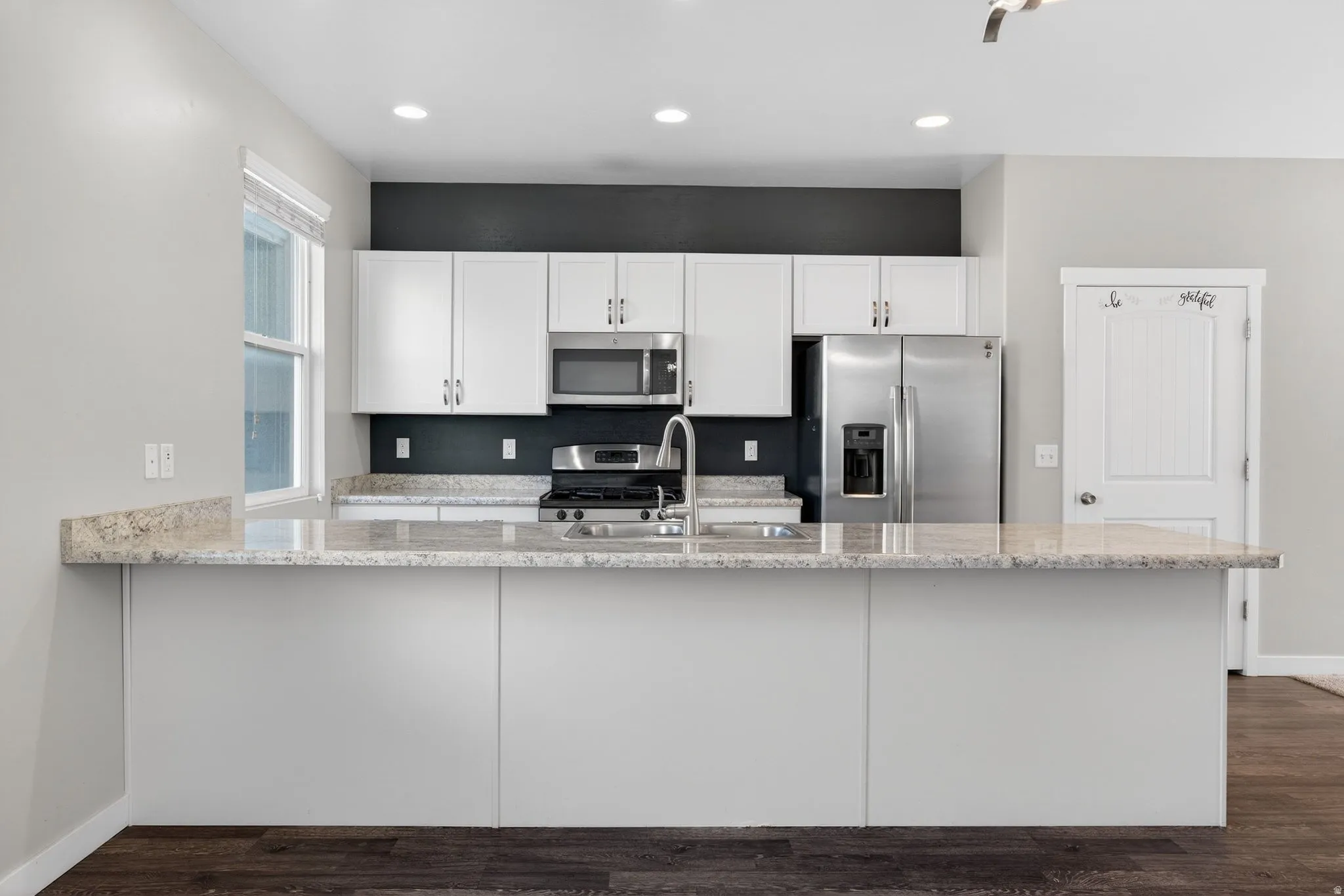 Kitchen with stainless steel appliances, light stone counters, white cabinets, a peninsula, and recessed lighting
