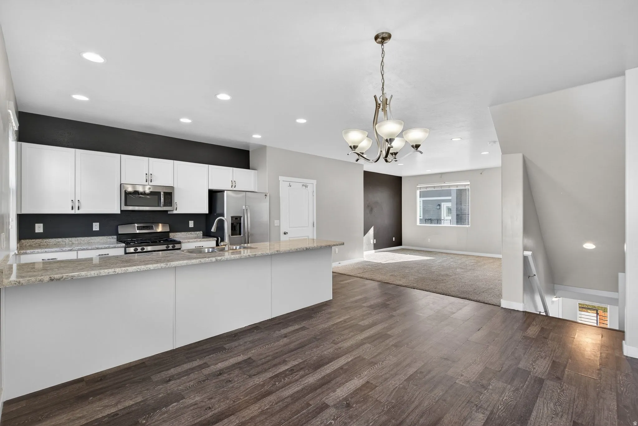 Kitchen with white cabinetry, open floor plan, stainless steel appliances, light stone counters, and suspended lighting