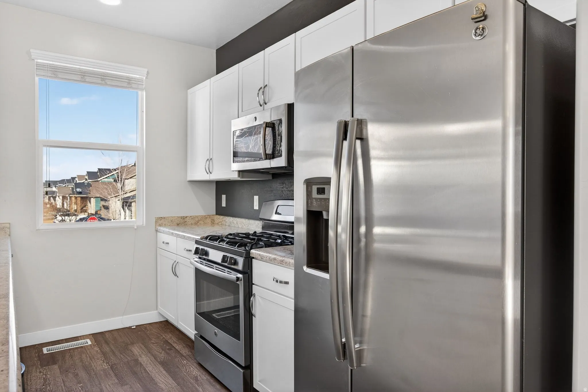 Kitchen with stainless steel appliances, white cabinets, and dark wood-style floors