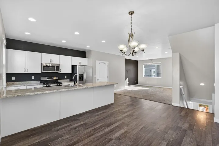 Kitchen with white cabinetry, open floor plan, stainless steel appliances, light stone counters, and suspended lighting